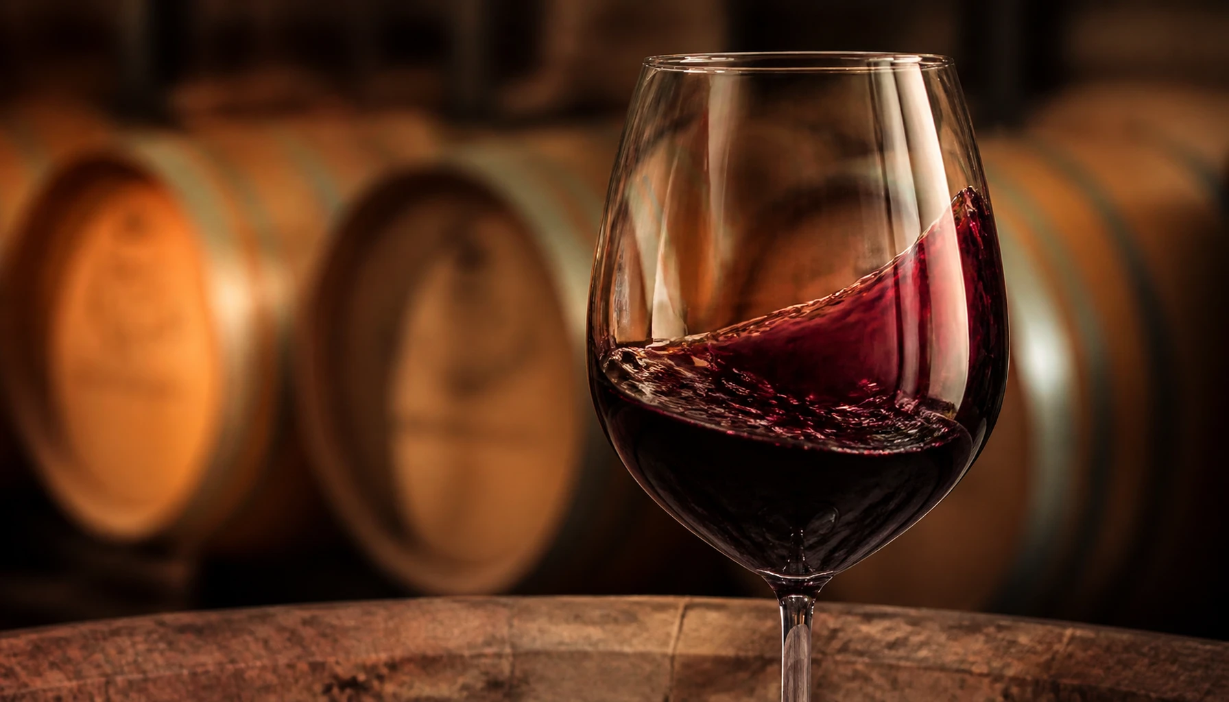 A dark Syrah mid-swirl, legs streaking the glass — the barrel room waiting its turn behind